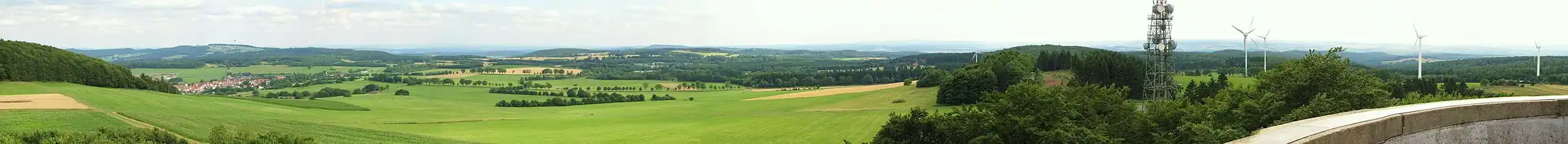 Blick vom Aussichtsturm auf dem Knüllköpfchen Richtung Osten und Süden. Links ist am Horizont der Eisenberg mit seinem Sendeturm zu erkennen. Davor liegt das Landstädtchen Schwarzenborn. In der Bildervergrößerung ist der bekannte Rimberg an der A 5 zu sehen. Der Berg mit seinem hohen Sendemast liegt über dem Teich am Horizont.
