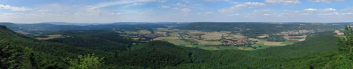 Blick von der Aussichtsterrasse des Heldrasteins. Der dominierende Höhenzug am Horizont in der linken Bildhälfte ist der Hohe Meißner. In der Bildmitte ist das Dorf Großburschla zu erkennen, weiter nach rechts folgen Heldra und Treffurt.