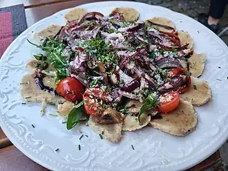 Semmelknödelcarpaccio mit Zwiebeln, Champignons, Rucola, Tomaten und Parmesan