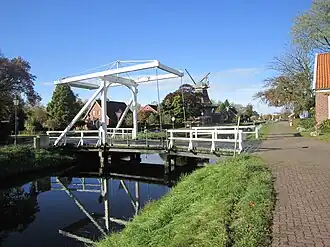 Szene in Großefehn: Eine der charakteristischen, weißen Klappbrücken am Kanal, Klinkerbauten und im Hintergrund eine Windmühle.